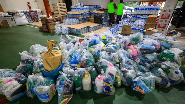 Foto de um lugar com doações, sacolas de produtos de limpeza e garrafa de água.