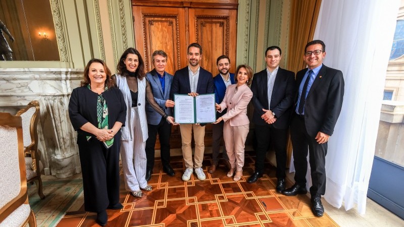 Foto de oito pessoas de pé segurando o decreto do programa.